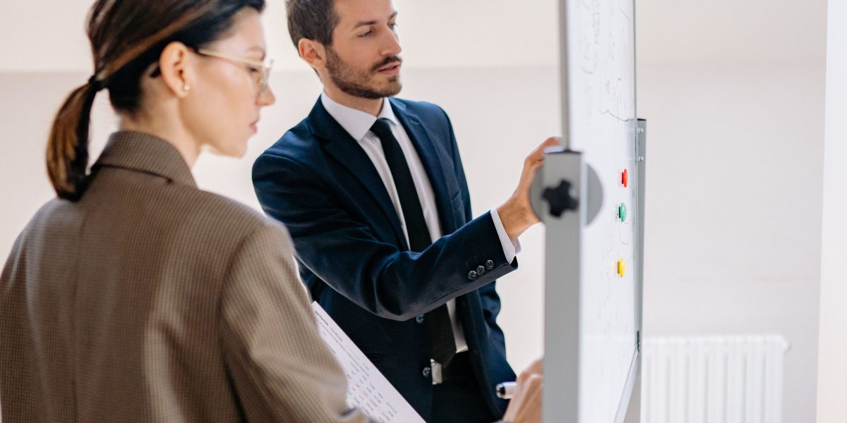 A team collaborates in an office, discussing and outlining different business strategies on a whiteboard.