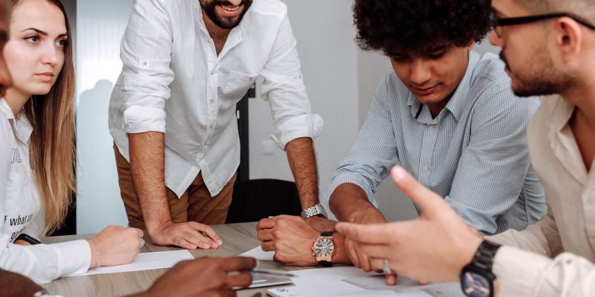 A diverse group of professionals in a meeting, actively discussing and comparing notes, symbolizing the effort to understand varying international regulations.